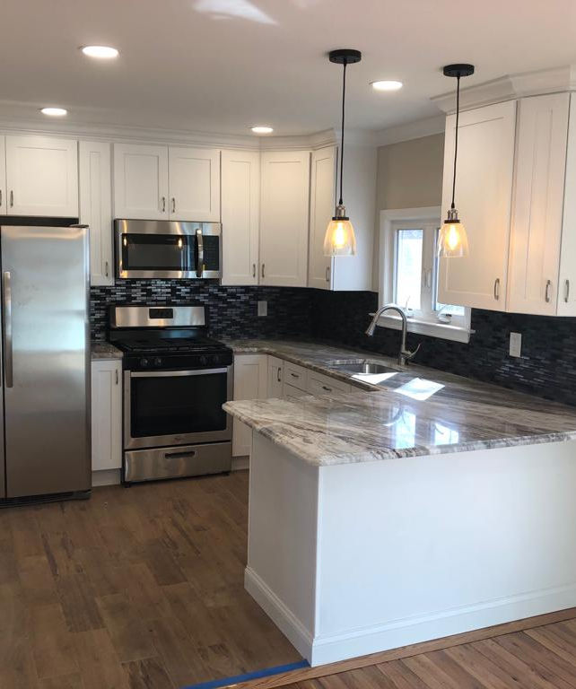 A bright, contemporary kitchen featuring white cabinets, stainless steel appliances, and a marble-topped island under pendant lights.