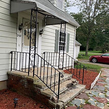 A house with a black wrought iron railing on stone steps leading to a covered front porch.