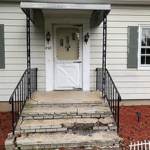 A house with a white door and black metal railings, featuring worn and cracked stone steps leading up to the entrance.