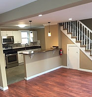 A bright, open-plan kitchen with hardwood floors and a staircase leading upstairs.