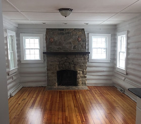 An empty room with hardwood floors and a stone fireplace centered between three windows.