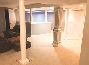 A spacious basement featuring white columns, a bar area, and carpeted flooring.