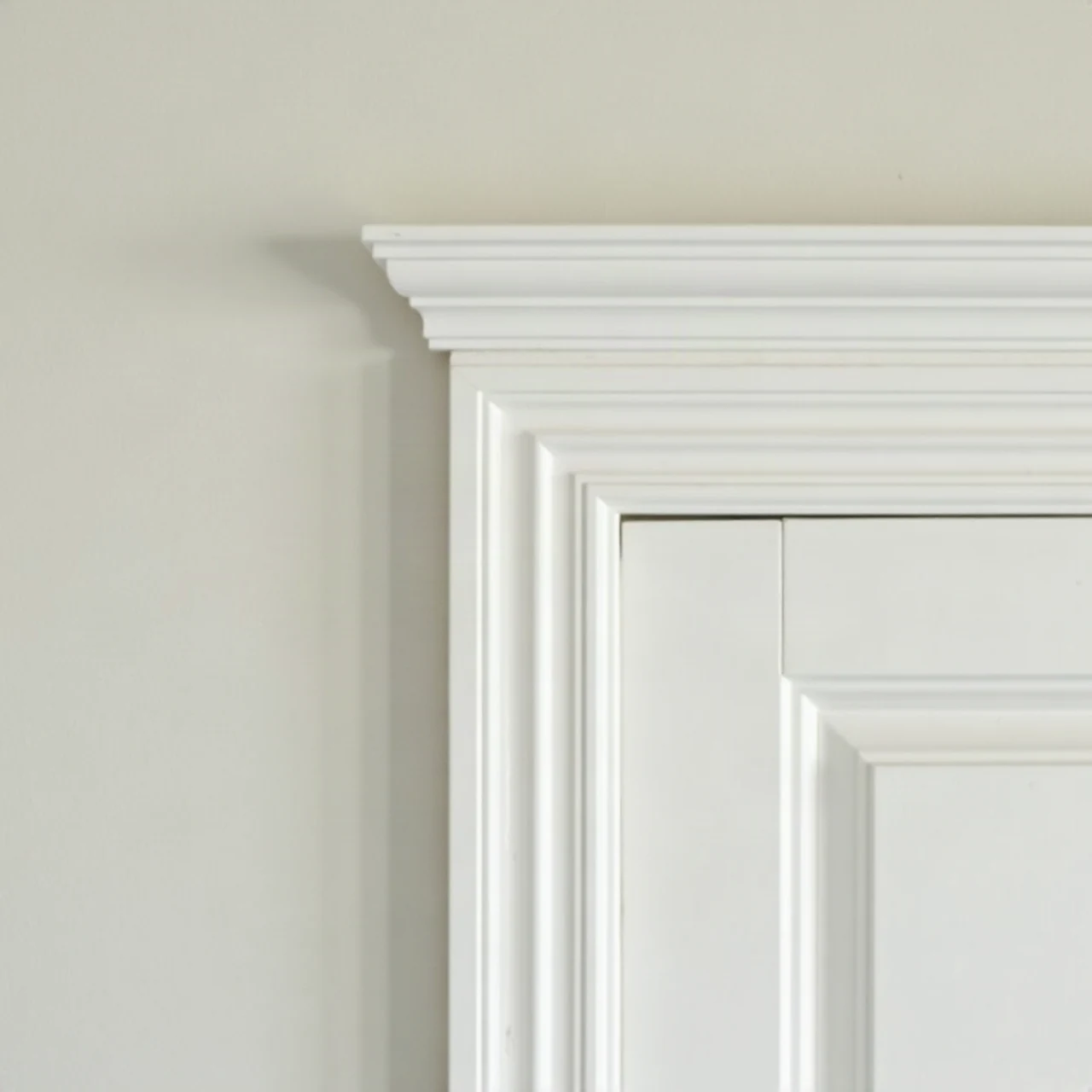 Close photograph of freshly painted white crown molding and door trim in a classic home interior, crisp lines, soft light, no text